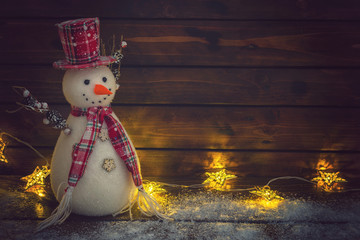 Christmas background with Christmas lights and snowman on the old wooden board