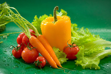Овощи - морковь, желтый перец, помидоры, листья салата на зеленом фоне Vegetables - carrots, yellow peppers, tomatoes, lettuce on a green background