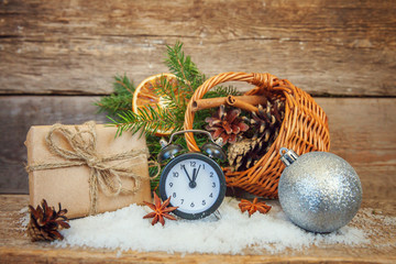Fototapeta na wymiar Christmas New Year composition winter objects gift box fir branch basket pine cones balls alarm clock on old shabby rustic wooden background. Xmas holiday december decoration copy space