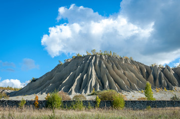 Slope of an abandoned slag heap covered ravines against the blue sky. Autumn landscape. Ruins on ex...