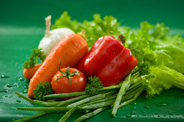 Овощи - морковь, помидоры, лук, паприка, салат, петрушка, зеленый лук на зеленом фоне Vegetables - carrots, tomatoes, onions, paprika, lettuce, parsley, green onions on a green background