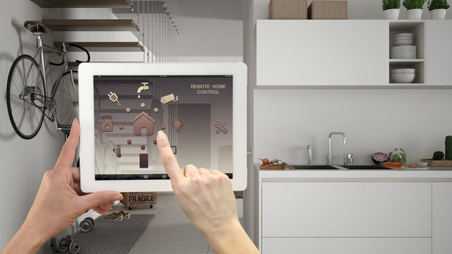 Smart remote home control system on a digital tablet. Device with app icons. Blurry interior of minimalist kitchen with stairs in the background, architecture design