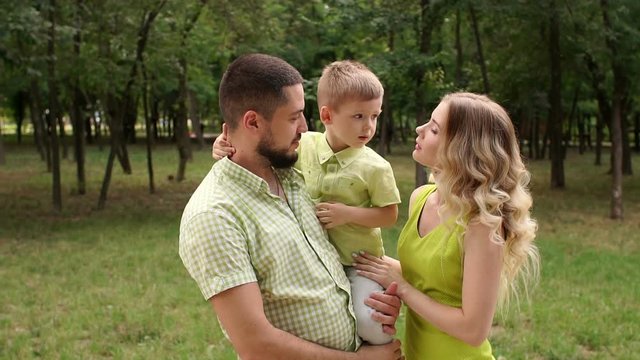 Portrait of a beautiful happy family with a small child outdoors on the background of green trees. A young mother with long blonde hair walks with her husband and son in a summer Park.