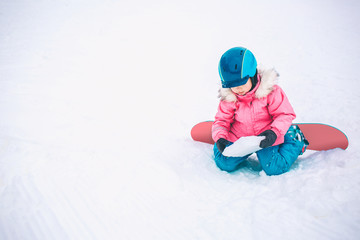 Fototapeta na wymiar Snowboard Winter Sport. Little kid girl playing with snow wearing warm winter clothes. Winter background