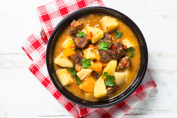 Goulash with meat and vegetables on white wooden table.