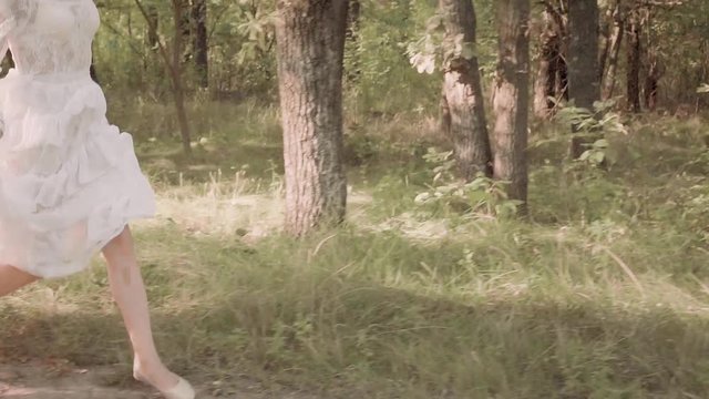 running bride in the forest escapes from the monster and killer. escaped young attractive girl in elegant white vintage dress with a long vibrating train and flying dark wavy hair in slow motion
