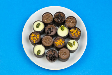 Chocolate candy on a white plate. Sweet beautiful candy lying on a plate on a bright color background.
