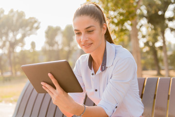 Fototapeta premium Young beautiful girl using tablet while sitting on the park bench
