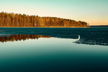 Beautiful autumn landscape. The first ice on a forest lake in the sunset.
