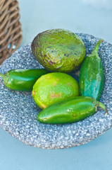 Top view, close distance of limes and jalapeno peppers in an artisan carved, stone , dish on display at a tropical, farmers market on an autumn day