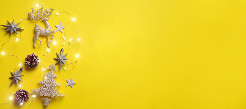 Christmas and new year concept. Greeting banner with copyspace. Shiny silver deer, stars, fir-tree, garland, bokeh on yellow background. Top view, flat lay