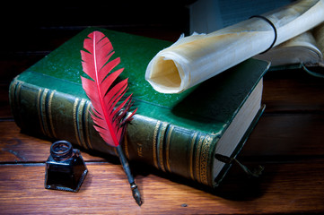 Red quill pen and a rolled papyrus sheet on a wooden table with old books