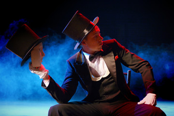 a young actor in a tuxedo holding a theatrical mask in a hat