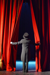 Actor in a tuxedo and hat looks behind the theater curtain