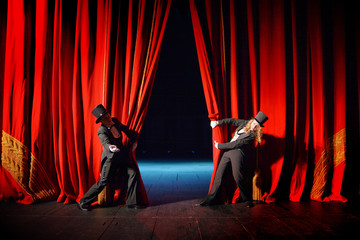 Actors in tuxedos and hats look behind the theater curtain