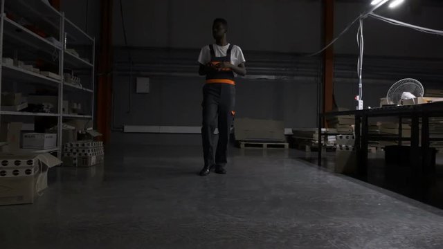 African american engineer walking forward in warehouse of LED light factory, full body, front view in slow motion