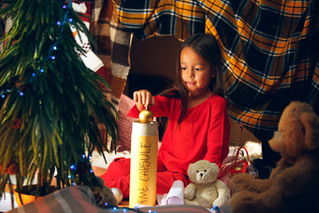 Merry Christmas and Happy Holidays. Cute little child girl writes the letter to Santa Claus near Christmas tree at home indoor. The holiday, childhood, winter, celebration concept