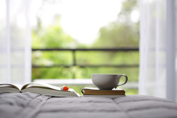 White cup and notebooks on bed with windows view