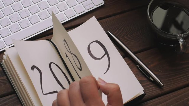 New Year 2019 is coming concept. Female hand flips notepad sheet on wooden table. 2018 is turning, 2019 is opening, toned