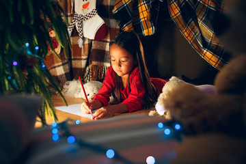 Merry Christmas and Happy Holidays. Cute little child girl writes the letter to Santa Claus near...