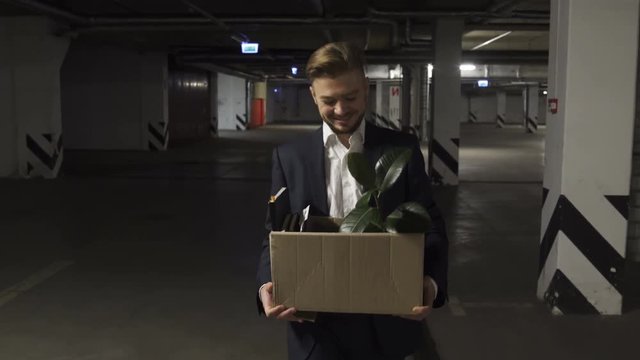 Very Emotional happy and smiling and then very sad Corporate worker gets fired and walking down parking lot with carton box and documents with a table flower. Mixed Emotions.