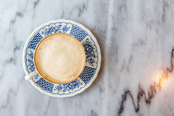 Coffee milk in a cup, rose patterned ceramic cup, on marble table in the morning light.