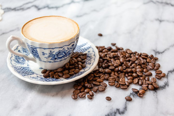 Coffee milk in a cup with coffee bean, rose patterned ceramic cup, on marble table in the morning light.