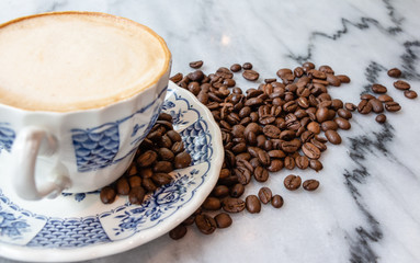 Coffee milk in a cup with coffee bean, rose patterned ceramic cup, on marble table in the morning light.
