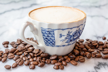 Coffee milk in a cup with coffee bean, rose patterned ceramic cup, on marble table in the morning light.