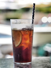 Glass of cola with ice cube, slice of lemon and straw in glass.