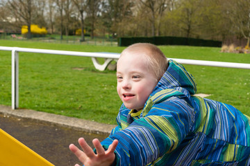 Defect,childcare,medicine and people concept- young boy with a down syndrome who is playing in a playground.