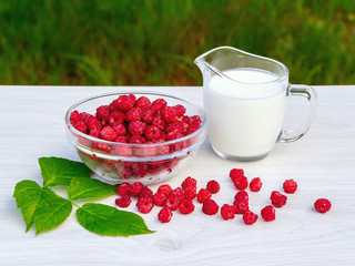 Fresh raspberries in a glass bowl and natural iogurt on a white wooden table. Healthy eating concept