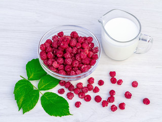 Fresh raspberries in a glass bowl and natural iogurt on a white wooden table. Healthy eating concept