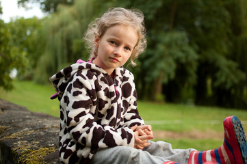 Portrait of a beautiful curly blue-eyed girl sitting on a background of green trees. Vacation in...