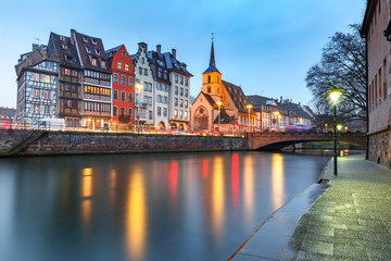 Picturesque Christmas quay and church of Saint Nicolas with mirror reflections in the river Ile during evening blue hour, Strasbourg, Alsace, France - obrazy, fototapety, plakaty