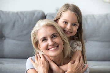 Portrait of cute little granddaughter piggyback smiling grandmother posing for family picture,...