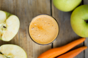 Homemade freshly squeezed apple and carrot juice in a clear glass with apple and carrot on a side from the top, flat lay