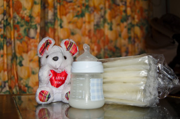 baby bottle with fresh expresed milk, frozen breastmilk in storage bags and soft toy mouse