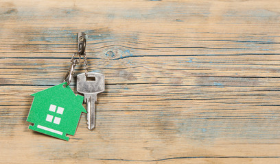 metallic key with house shaped key chain on wooden background