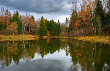 Cloudy autumn landscape with forest pond and trees.Dark stormy clouds in dramatic overcast sky.