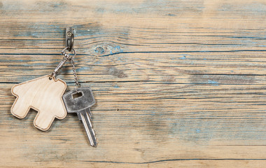 metallic key with house shaped key chain on wooden background