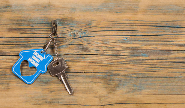 metallic key with house shaped key chain on wooden background