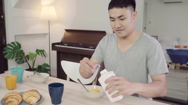 Happy Asian man having breakfast, cereal in milk, bread and drinking orange juice after wake up in the morning. Lifestyle man eating food at home concept.