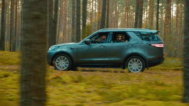 TRACKING Caucasian couple with a pet dog driving on a forest road in a modern SUV. 4K UHD
