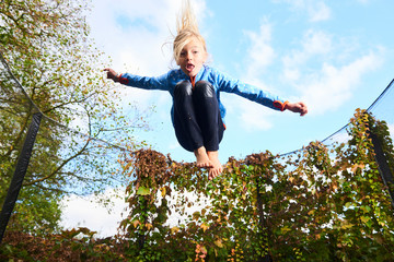 Child cute blond girl playing and jumping on trampoline with greenery background. Children are at a high risk of injury when they jump on trampolines