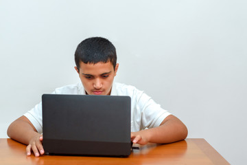 Teenager with laptop sitting at table and studying at home. Fashion portrait of teen black hair handsome boy in office. Young businessman using a laptop.
