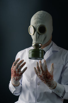 Evil and creepy medical experiment concept, a scary doctor in gas mask wearing bloody gloves on dark background