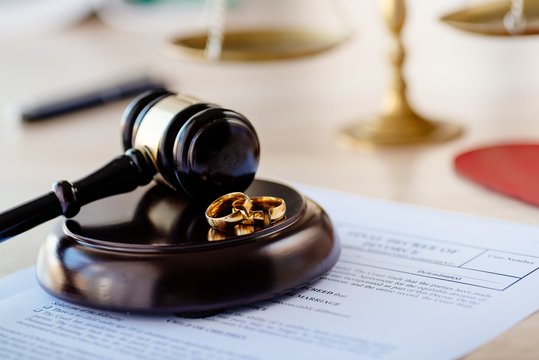 Divorce decree in and two broken wedding rings on judge gavel.