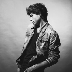 Portrait of Handsome Young Man. A Men in a Denim Jacket Posing on a Gray Background. Black and White Photo