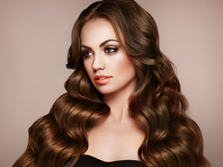 Brunette Girl with Long Healthy and Shiny Curly Hair. Care and Beauty. Beautiful Model Woman with Wavy Hairstyle. Make-Up and Black Dress